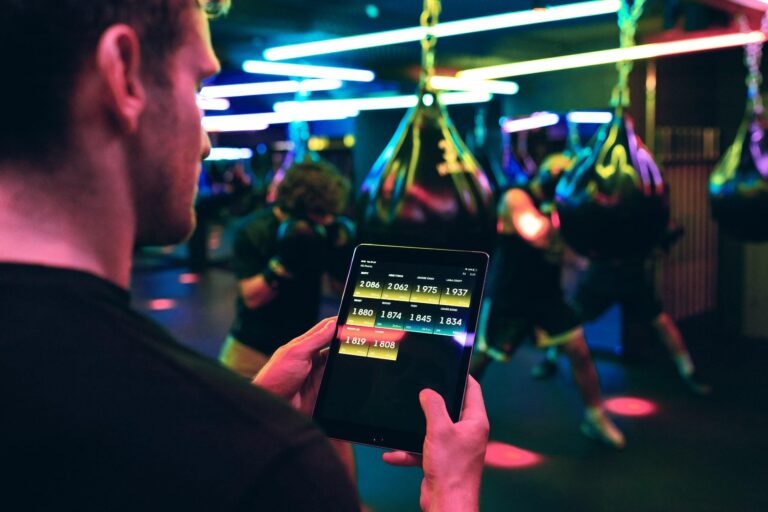 Coach viewing a live performance leaderboard on a tablet in a neon-lit boxing gym, representing sports data and gamification.